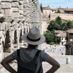 women in blue crew neck t-shirt and brown fedora hat standing near brown concrete ruined buildings