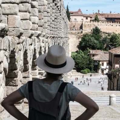 women in blue crew neck t-shirt and brown fedora hat standing near brown concrete ruined buildings