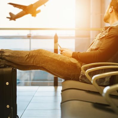 man in departures at airport waiting for flight and plane taking off in distance